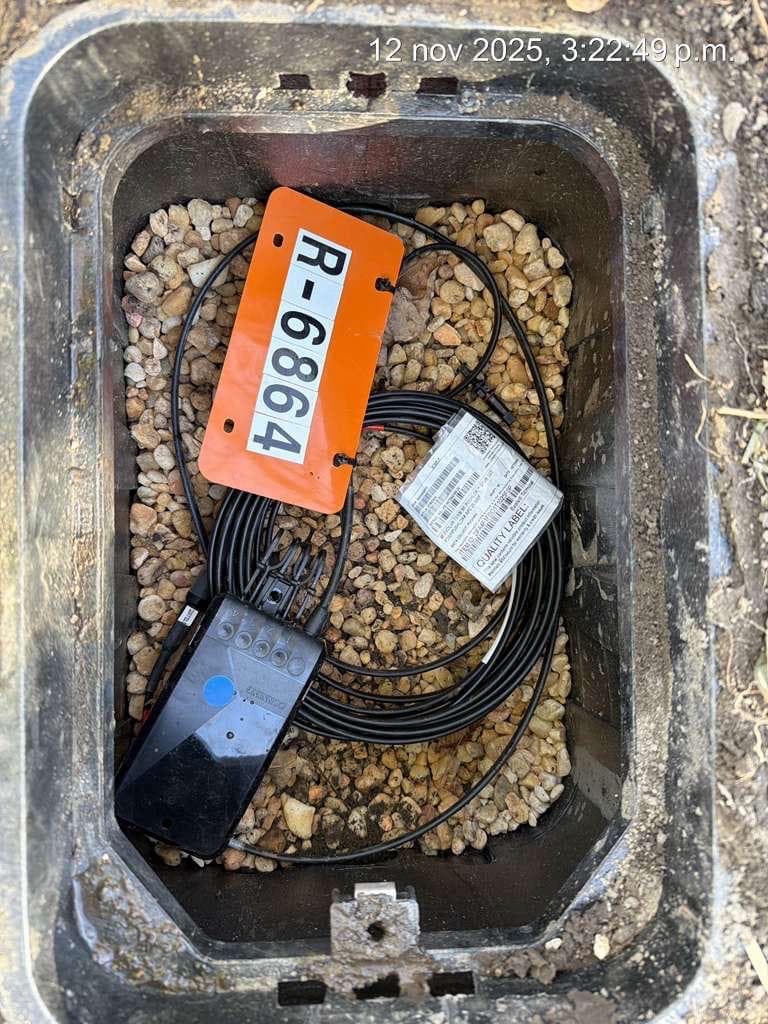 Open handhole with a fiber terminal, coiled drop cable and a numbered location tag on a gravel base