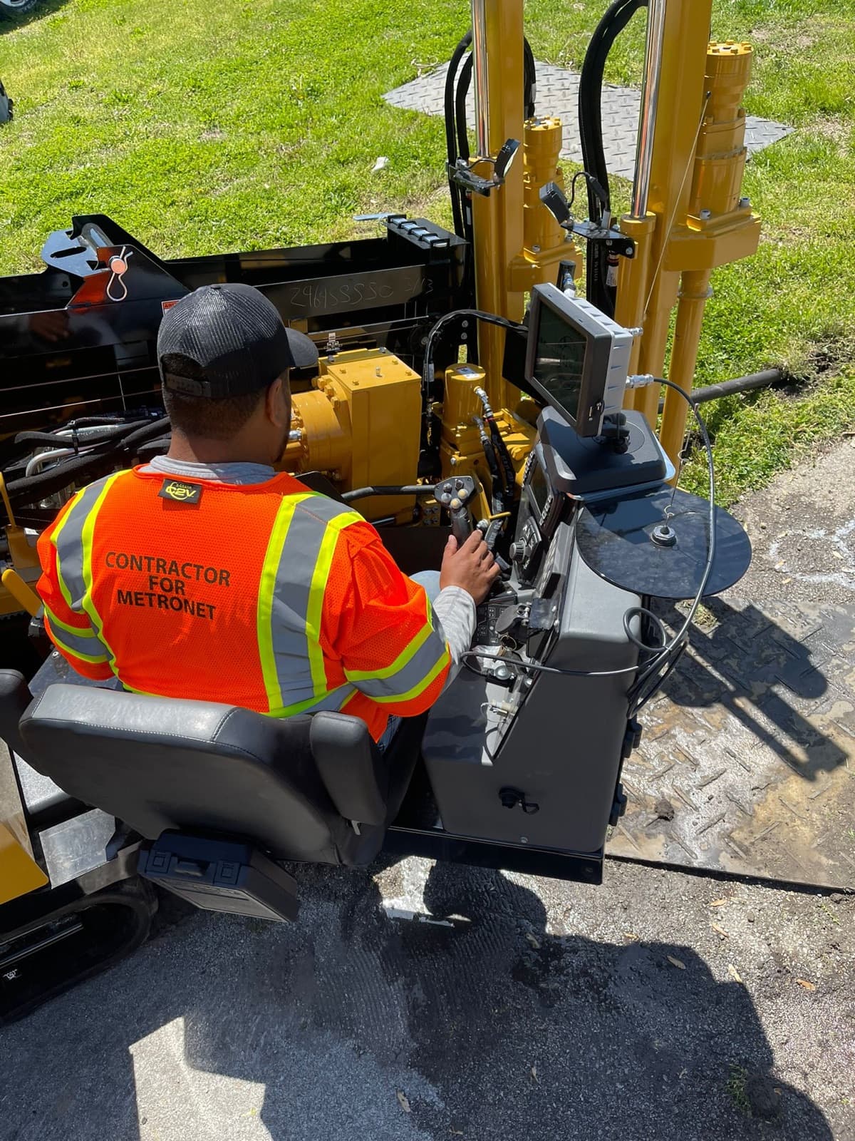 Drill operator in an orange contractor vest at the controls of a directional drill
