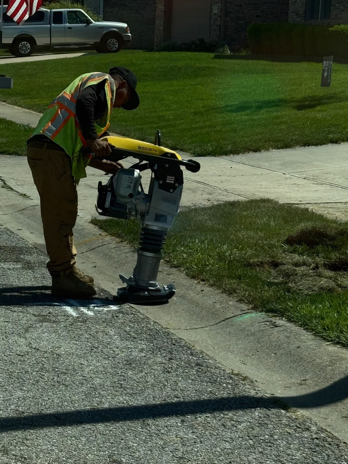 Crew member compacting soil with a rammer next to a sidewalk during site restoration