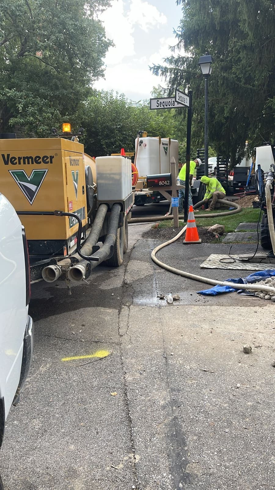 Vacuum excavation trailer and crew working a pothole beside a driveway